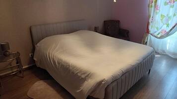 A bedroom with a bed, a nightstand, a chair, a lamp, and a window with curtains.