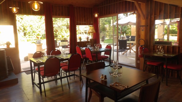 An indoor dining area with wooden tables and red chairs, large windows, and hanging light fixtures.
