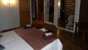 A bedroom with a bed, a wooden door, a small table, and a stone wall.