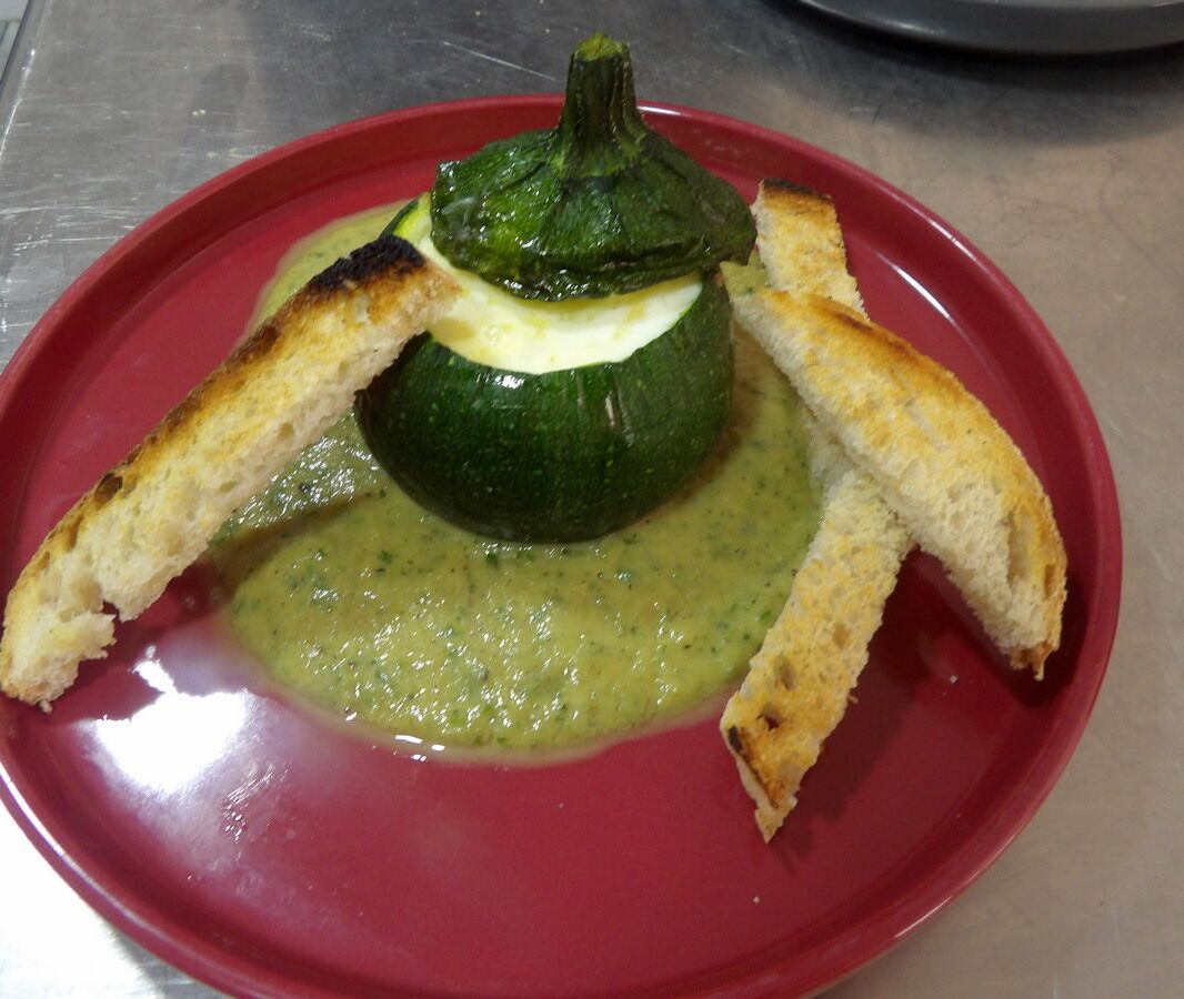 A stuffed zucchini with grilled bread on a red plate.