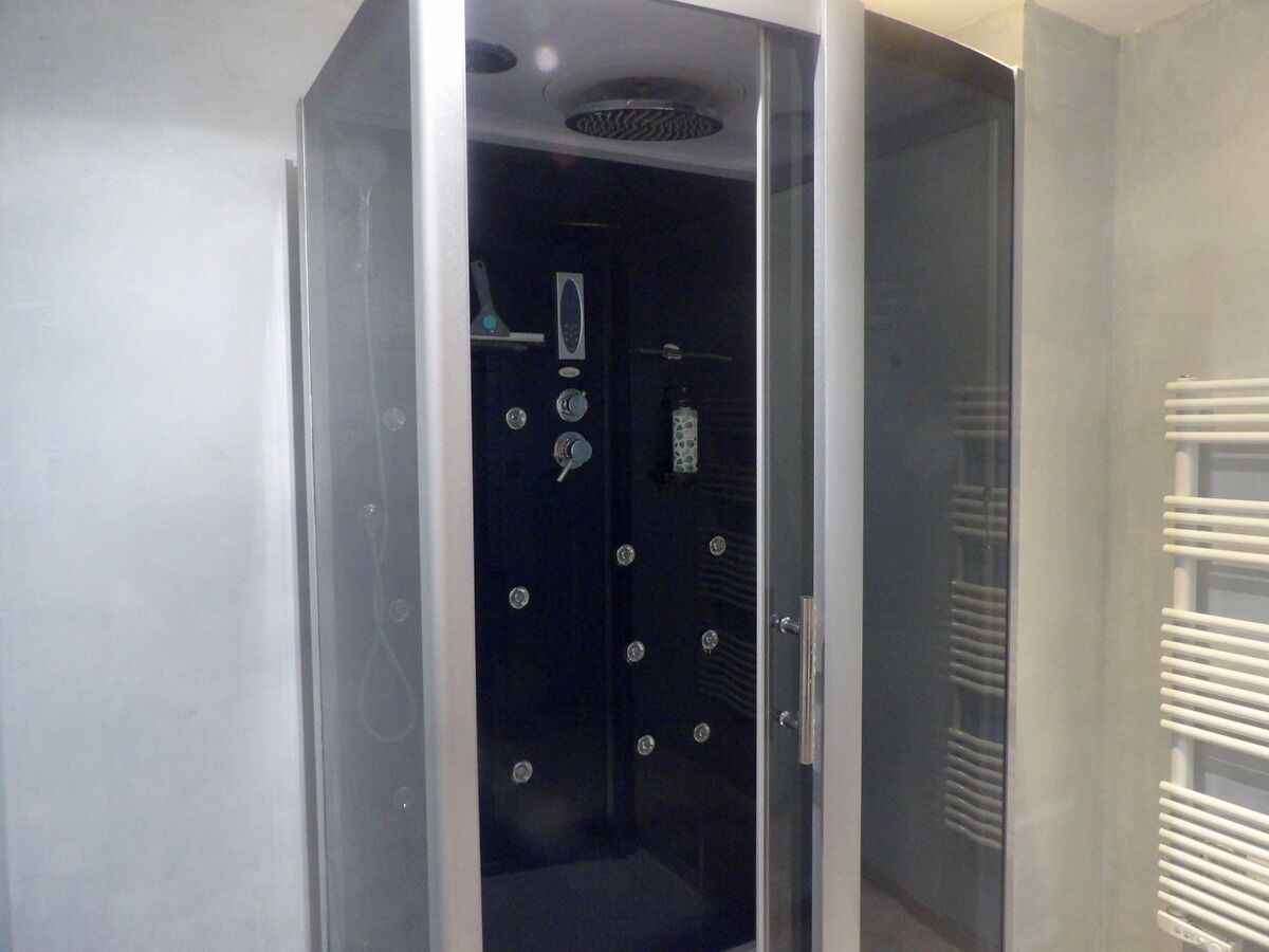Une salle de bain moderne dotée d’une paroi de douche en verre, d’une douche avec panneau de commande et d’un porte-serviettes.