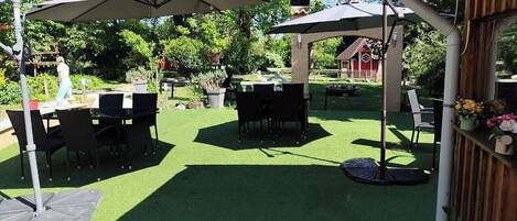 An outdoor patio with artificial grass, tables, chairs, and umbrellas.