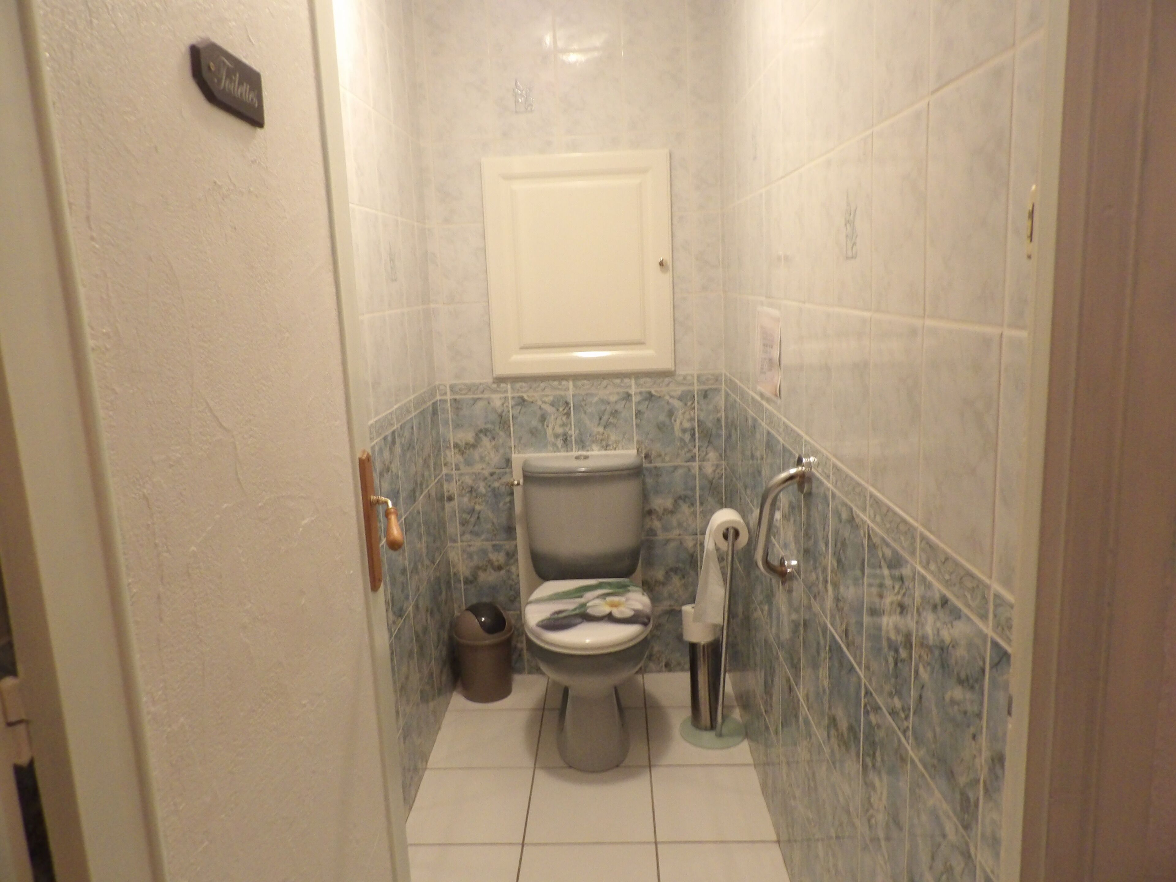 A bathroom with a toilet, a trash bin, a towel dispenser, and a toilet paper holder.