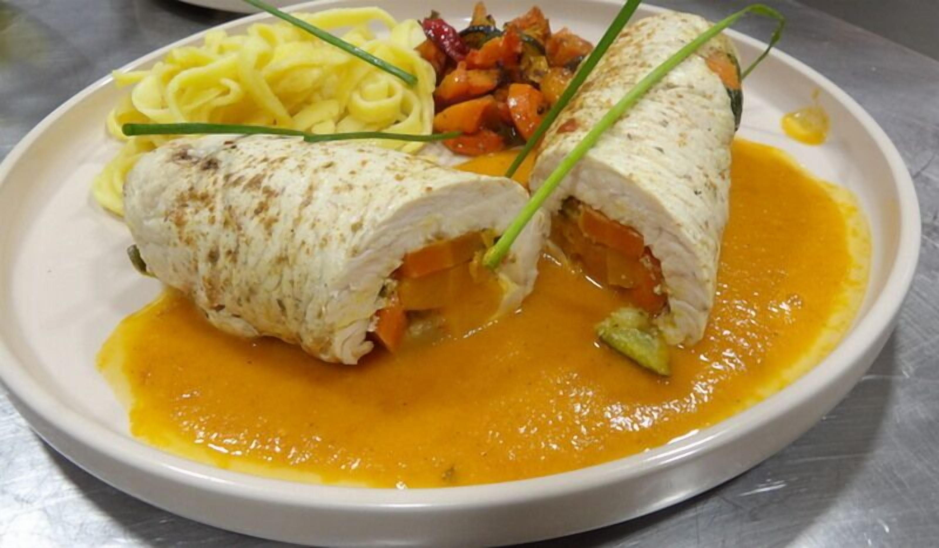 Une assiette contenant un plat de viande enroulée, des légumes et une sauce jaune.