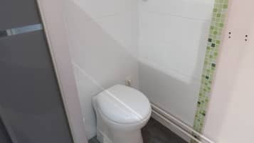 A small, white toilet in a corner with a green-tiled shower area.