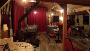 A restaurant with wooden interiors, red curtains, and multiple dining tables set for guests.