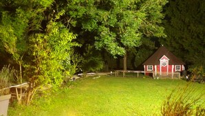 A red house with a white door and a small porch, surrounded by a grassy yard and trees.