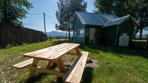 Ett picknickbord av trä med bänkar, placerat på en gräsyta intill en liten, grön byggnad med ett tak av metall.