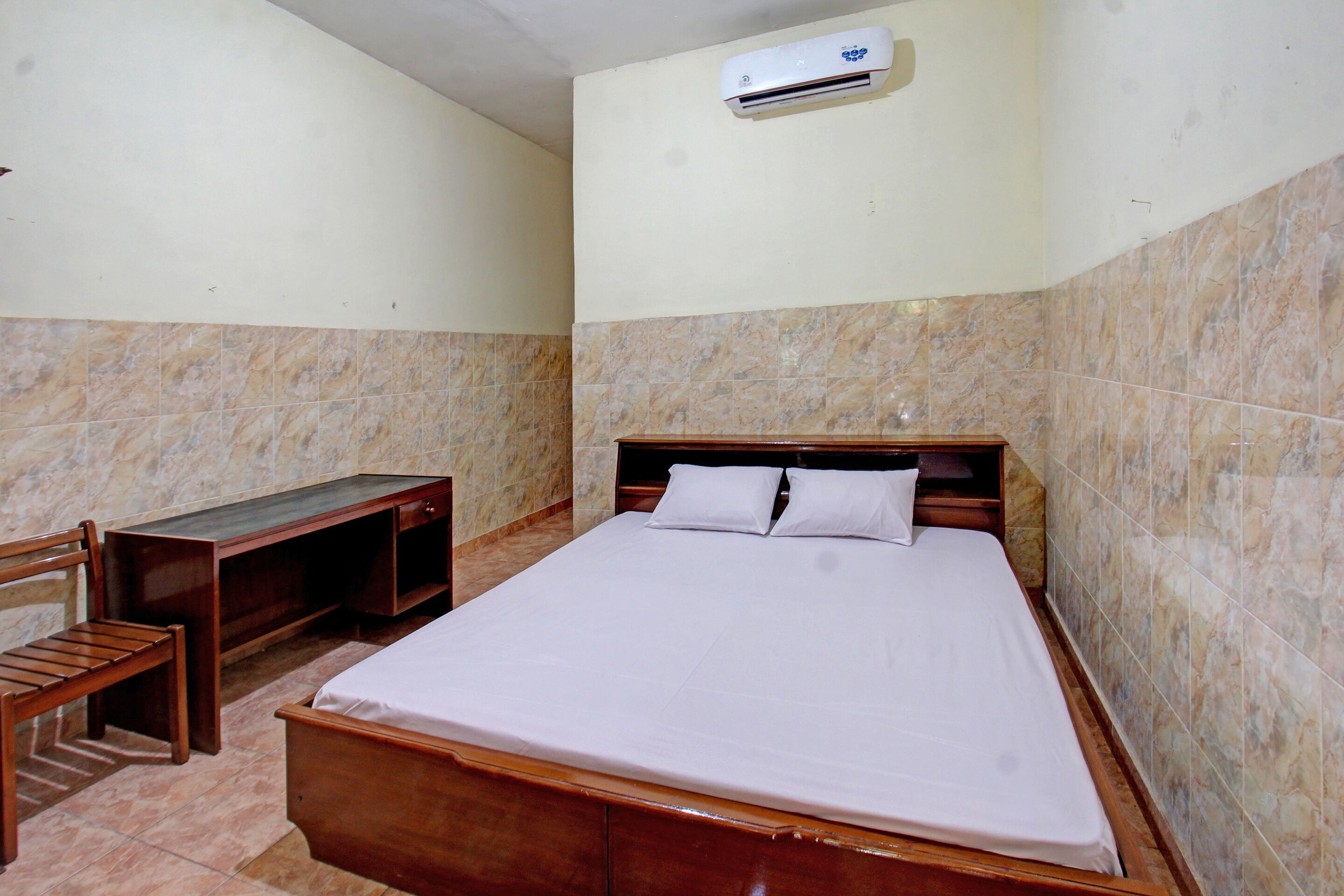 A bedroom with a bed, a wooden desk, and an air conditioning unit on the wall.