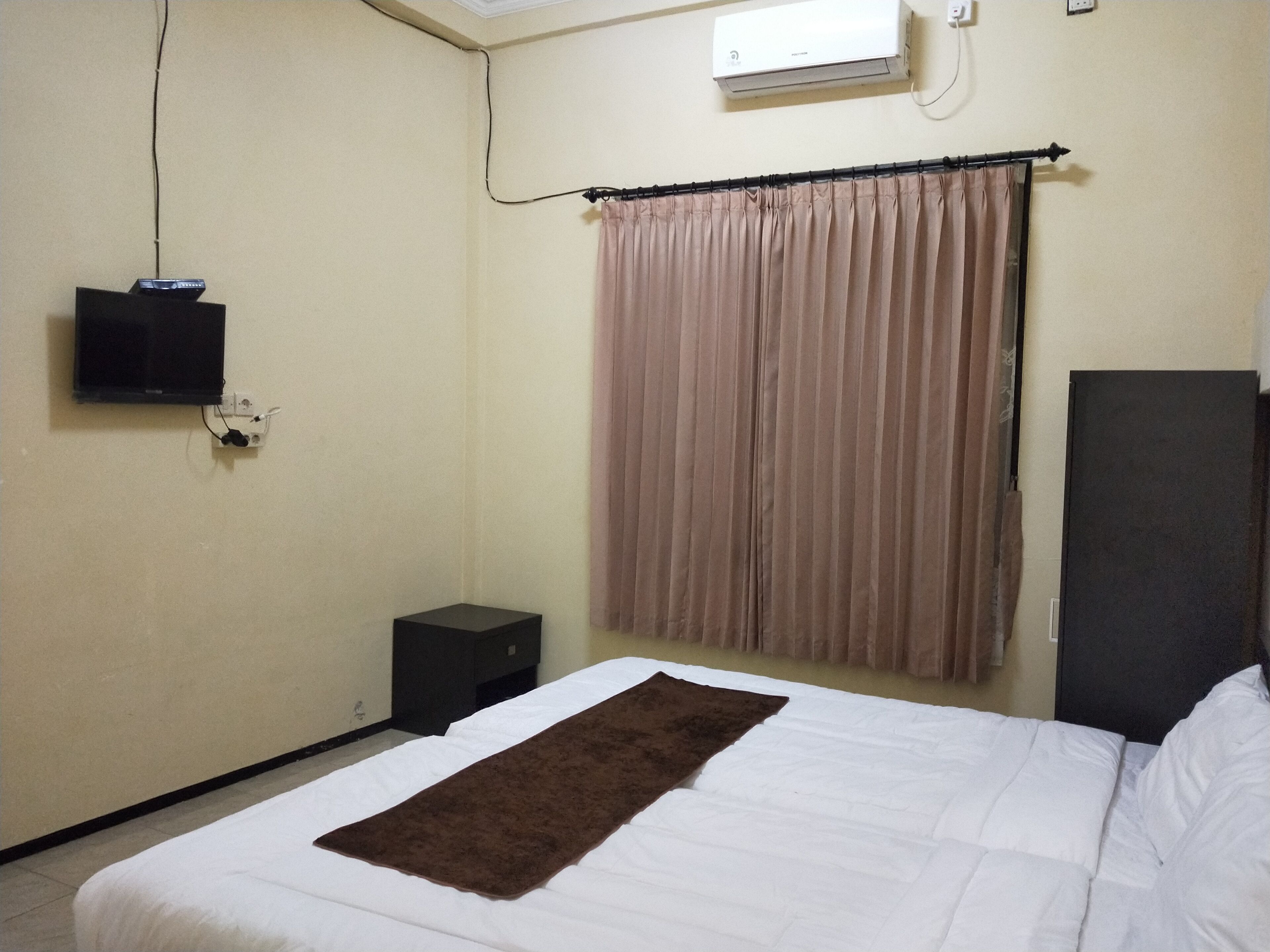 A hotel room with a bed, a television mounted on the wall, a small table, and a window with curtains.