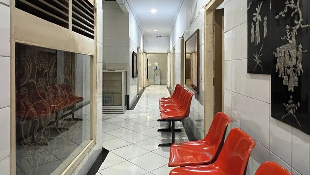 A hallway with red chairs lined up, a ceiling fan, and a glass door with floral patterns. - OYO 92675 Hotel Rosna (Makassar)