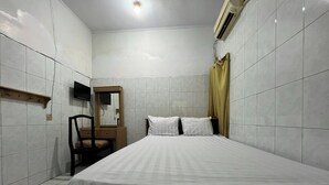A small, clean room with a bed, a chair, a wooden shelf, a mirror, and an air conditioning unit. - OYO 92675 Hotel Rosna (Makassar)