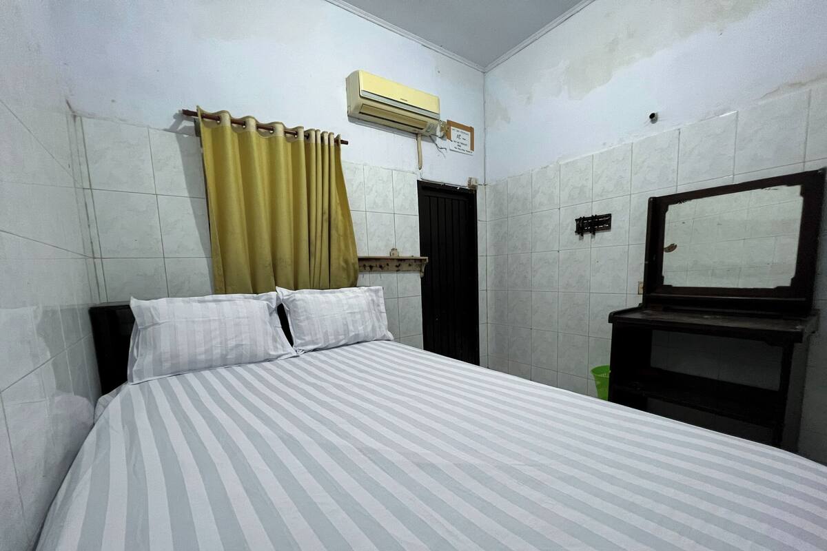 Quarto com cama, espelho, janela com cortinas e ar condicionado.