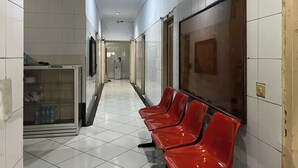A corridor with white tiled walls, a tiled floor, and red chairs along one side. - OYO 92675 Hotel Rosna (Makassar)