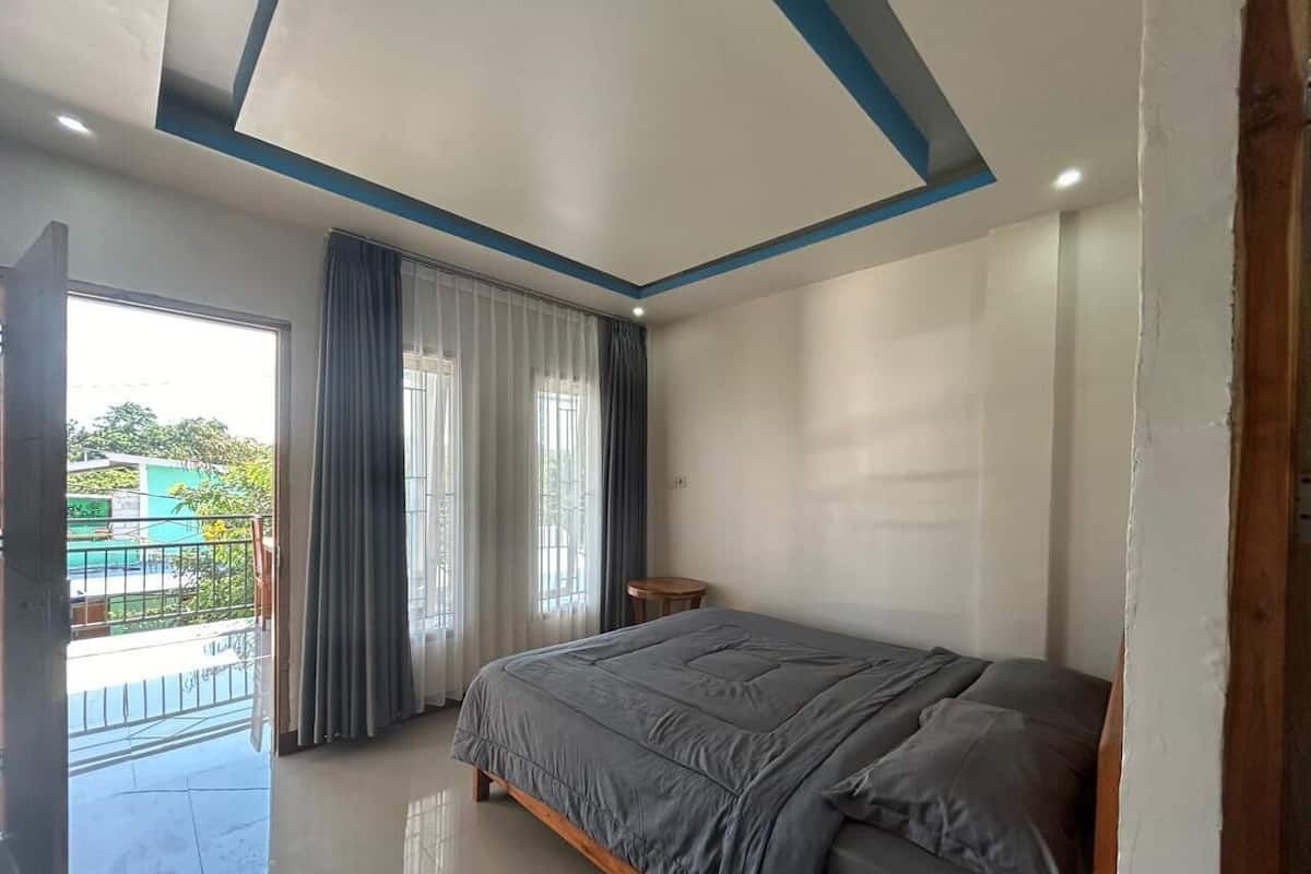 A bedroom with a large bed, a small table, and a view of a balcony.