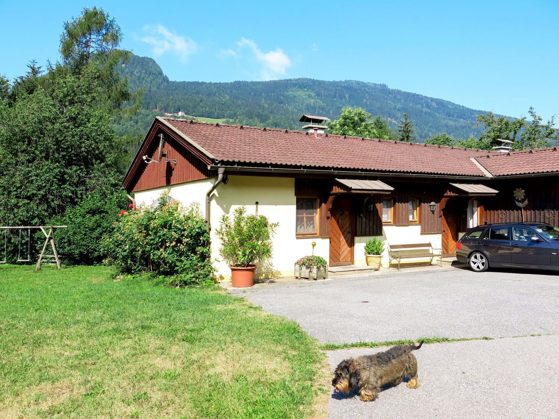 A traditional chalet with a sloped roof, a wooden front door, and a car parked in the driveway.