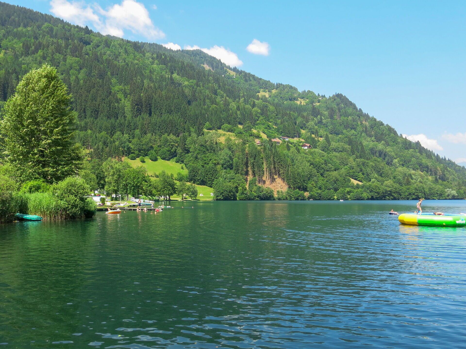 A lake surrounded by forested hills with boats and a green inflatable raft.
