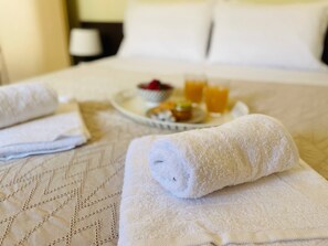 A neatly made bed with a quilted pattern, two rolled white towels, and a tray with breakfast items including orange juice and pastries.