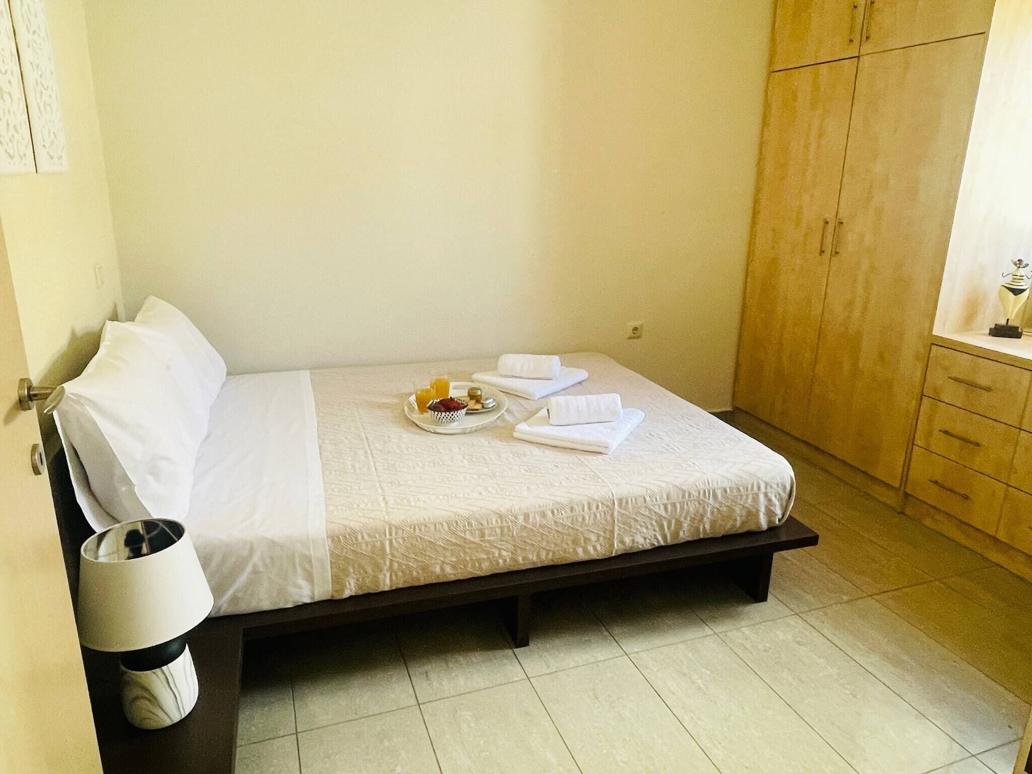 A neatly made bed with a tray of breakfast items, a bedside lamp, and a wardrobe in a hotel room.