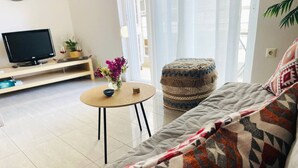 A living room with a sofa, a round coffee table, a television, and a small side table with a vase of flowers. - Cozy Nest - 2min To Beach, 6min Walk To (Chania)
