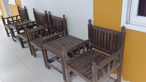 A row of wooden chairs and tables against a yellow wall, with a window to the right. - Hotel O Wisma Parakita Syariah Near RS Faisal Patalasang (Pattallassang)