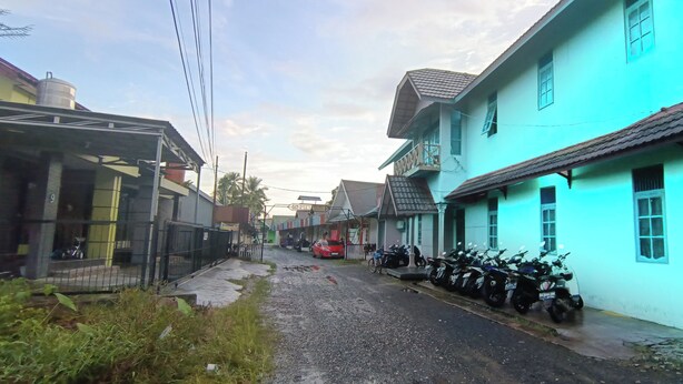 A narrow street lined with buildings, a parked motorcycle, and a red car. - Hotel O Wisma Parakita Syariah Near RS Faisal Patalasang (Pattallassang)