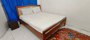 A single bed with a wooden frame and white bedding in a room with a tiled floor and a red floral rug. - Hotel O Wisma Parakita Syariah Near RS Faisal Patalasang (Pattallassang)