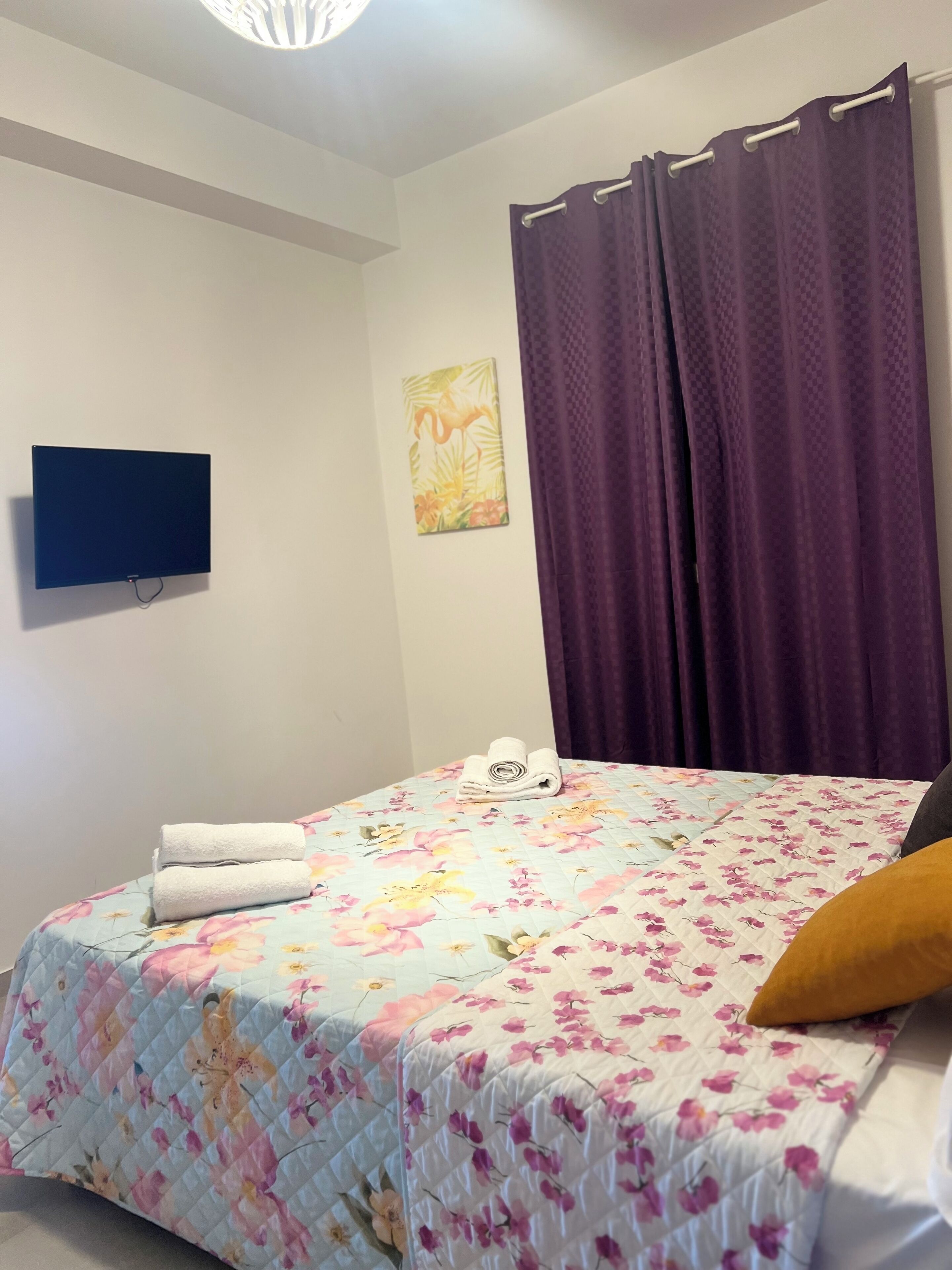 Une chambre à coucher avec un lit, un téléviseur à écran plat, un tableau et des rideaux violets.