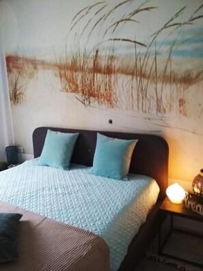 A bedroom with a bed, pillows, a nightstand, and a wall painting.