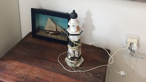 Quadre amb un vaixell a la platja, una taula petita amb una maqueta de far i una presa elèctrica a la paret.