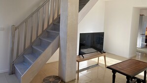 A staircase with metal railings, a flat-screen TV on a stand, and a small wooden table. - Petite Maison Avec Terrain Entre Route, Vignes et Lavande (Sainte-Cécile-les-Vignes)
