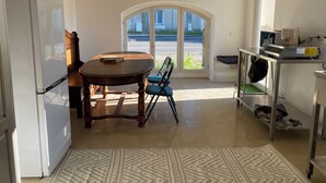 A kitchen with a dining table, chairs, a refrigerator, and a view through a glass door. - Petite Maison Avec Terrain Entre Route, Vignes et Lavande (Sainte-Cécile-les-Vignes)