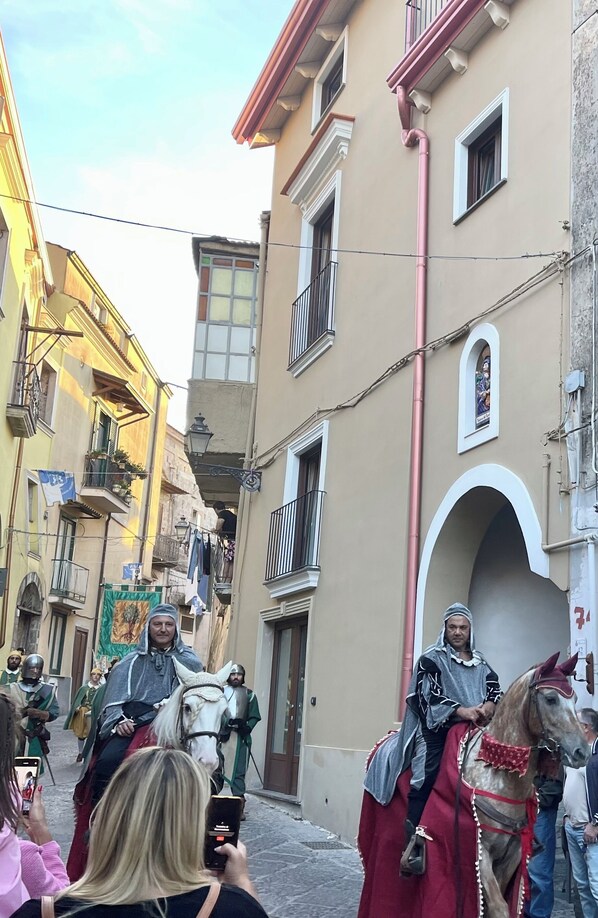 Una calle estrecha flanqueada por edificios, una persona a caballo y varias personas tomando fotografías.