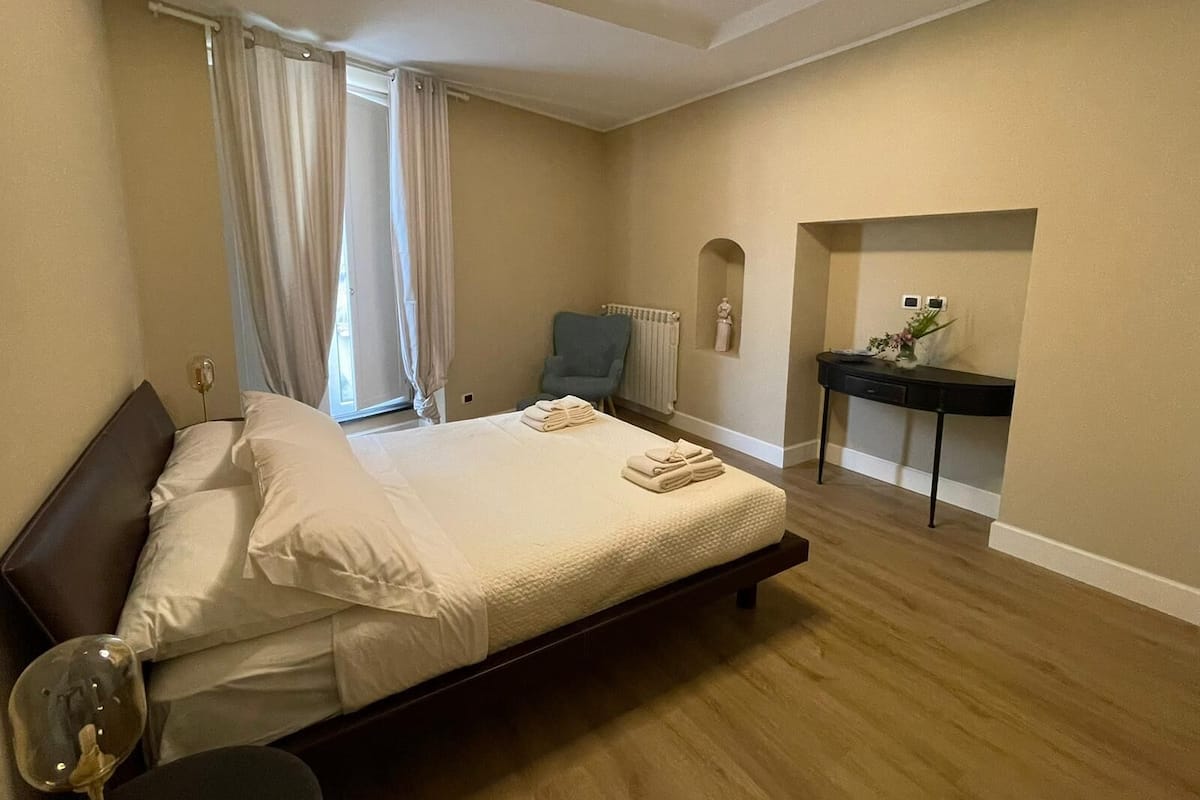 A bedroom with a bed, a chair, a desk, and a radiator.