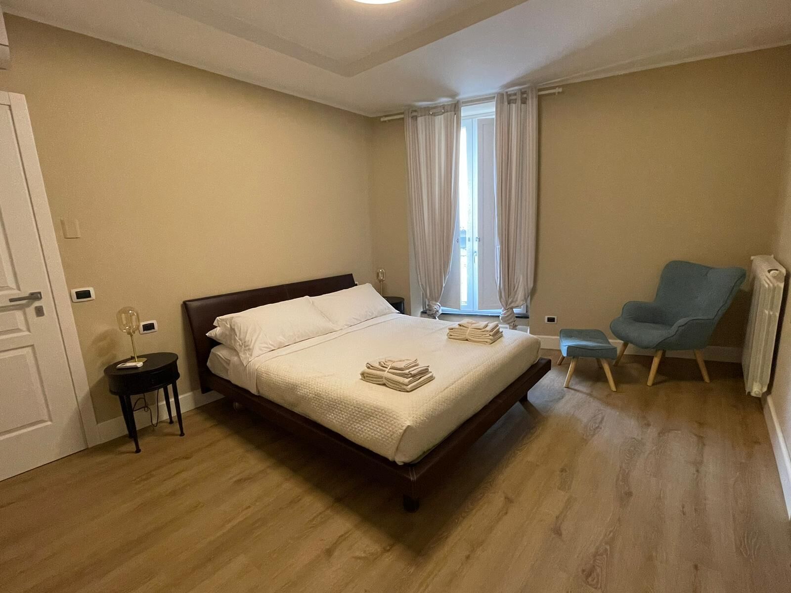 Una habitación de hotel con una cama, una silla, una mesita y un ventanal con cortinas.