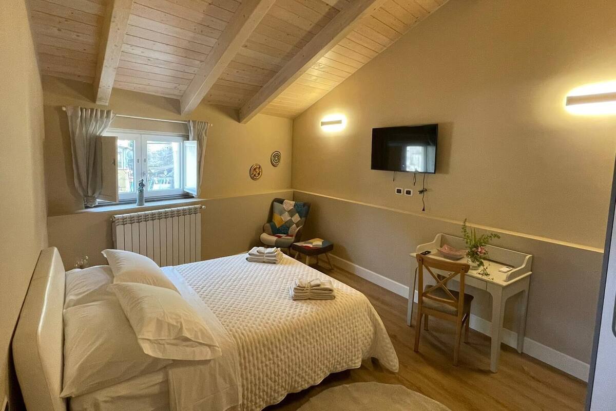 A bedroom with a bed, a desk, a chair, a TV, and a window with curtains.
