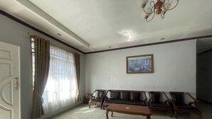 A spacious room with a large window, a sofa set, a wooden coffee table, and a painting on the wall. - Hotel O Bahagia Homestay SyariahNearMonument Park City Sand Pengaraian (Pasir Pengaraian)