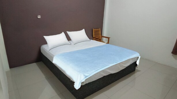 A single bed with a white mattress and a blue blanket, a wooden chair, and a brown wall. - Hotel O Wisma Deli Syariah Near RSUD Nene Mallomo Sidenreng Rappang (Pangkajene)