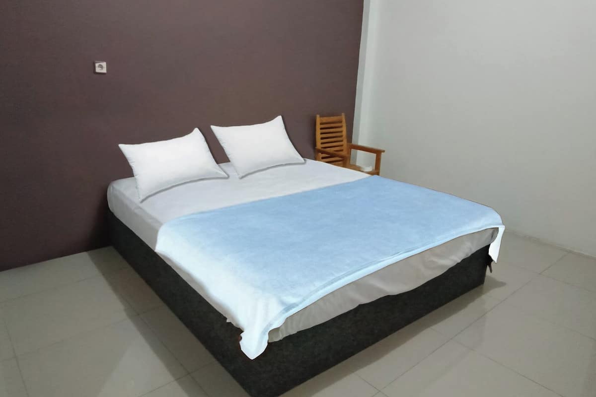 A single bed with a white mattress and a blue blanket, a wooden chair, and a brown wall.
