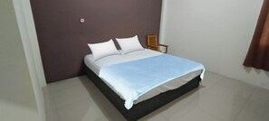 A single bed with a white mattress and a blue blanket, a wooden chair, and a brown wall. - Hotel O Wisma Deli Syariah Near RSUD Nene Mallomo Sidenreng Rappang (Pangkajene)
