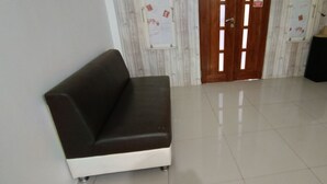 A room with a dark brown sofa, a wooden door with glass panels, and a tiled floor. - Hotel O Wisma Deli Syariah Near RSUD Nene Mallomo Sidenreng Rappang (Pangkajene)