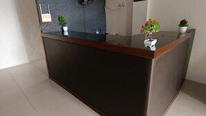 A modern reception desk with a dark wooden top and a glass panel. There are two potted plants on the desk, one with green foliage and the other with red leaves. - Hotel O Wisma Deli Syariah Near RSUD Nene Mallomo Sidenreng Rappang (Pangkajene)