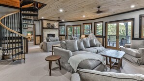 A spacious living room with a curved staircase, large windows, and a fireplace. - Lakefront Innisfree | Blue Ridge, GA (Blue Ridge)