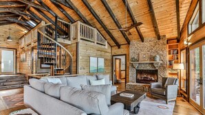A spacious living room with a fireplace, a staircase, and a bookshelf. - Lakefront Innisfree | Blue Ridge, GA (Blue Ridge)