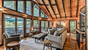 A spacious cabin with large windows, a cozy living area with a sofa and chairs, and a wooden ceiling. - Lakefront Innisfree | Blue Ridge, GA (Blue Ridge)