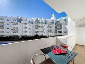 Un balcon avec une table dressée pour le dîner, offrant une vue sur un immeuble moderne doté de nombreux balcons et sur un ciel dégagé.