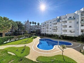 A swimming pool surrounded by a brick pathway, with white apartment buildings in the background.