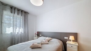 Een netjes opgemaakt slaapkamer met een bed, nachtkastjes, een lamp en een raam met gordijnen.