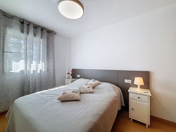 Une chambre à coucher bien rangée, avec un lit, des tables de chevet, une lampe et une fenêtre avec des rideaux.