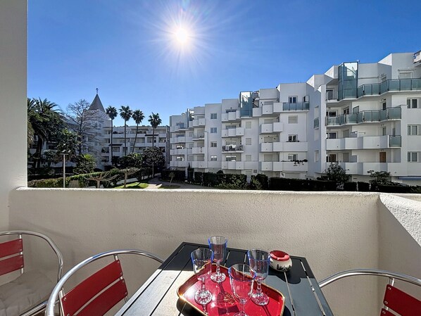 A balcony with a table set for dining, overlooking modern apartment buildings and a clear sky.